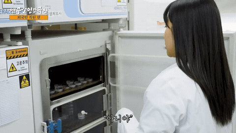 연구실 장비 앞에서 흰 가운을 입은 사람이 기기를 다루는 장면