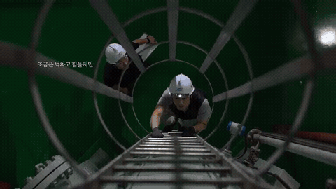 안전모를 쓴 작업자가 원형 통로 안쪽 사다리에서 작업하는 장면