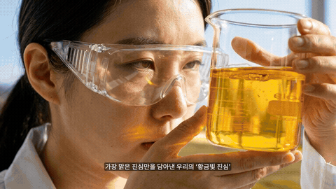 보안경을 쓴 연구원이 황금빛 액체가 담긴 비커를 얼굴 옆으로 들어 올린 클로즈업과, 소금호수 위 나무배에 앉아 같은 비커를 든 컷