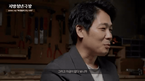 공구가 걸린 어두운 작업실에서 재킷 차림 남성이 인터뷰하고 좌상단에 프로그램 제목, 아래에 한글 자막이 붙은 장면