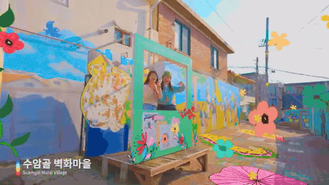 벽화마을 포토존 실사에 붓터치 꽃 그래픽이 그려지고 여행객이 손을 흔드는 장면
