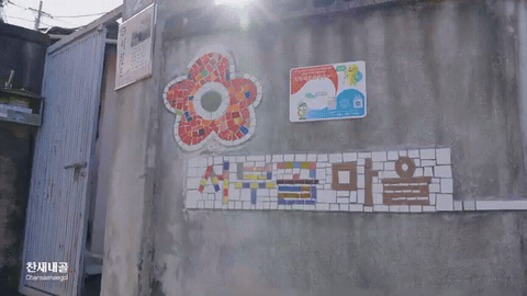 옛 마을 담벼락의 타일 벽화에서 공원 부지를 내려다보는 항공 장면으로 넘어가는 컷