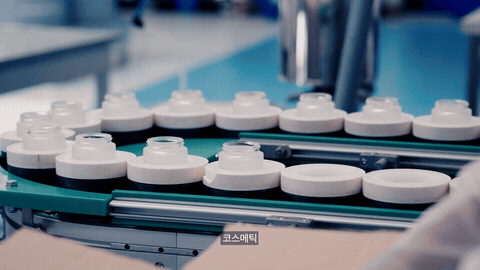 파란 장갑 손이 컨베이어 위 용기를 정리하는 생산 라인 장면